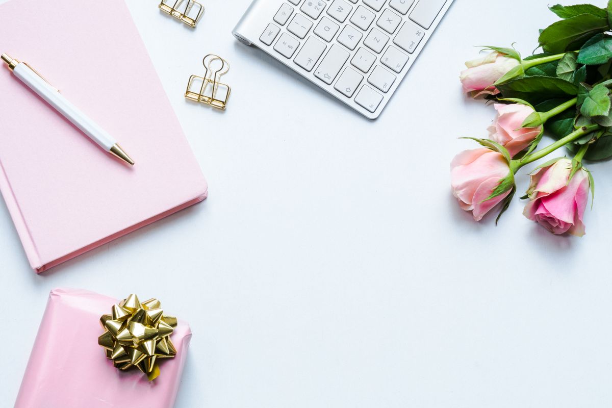 Beautiful office desk setup with roses, a gift, notebook, and keyboard for a stylish workspace.