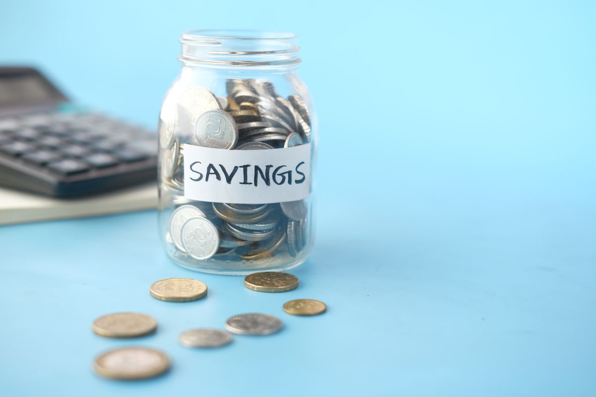 Glass jar labeled 'Savings' filled with coins, beside a calculator on a blue background.