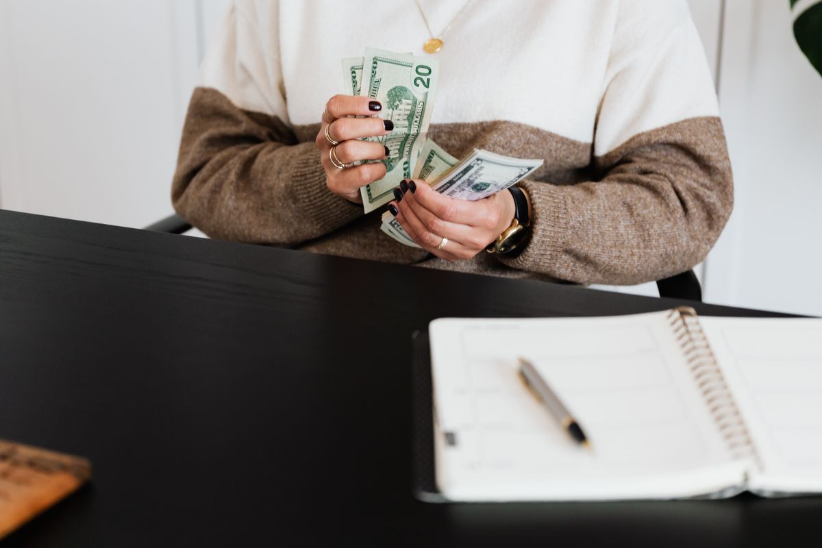 Close-up of an adult counting dollar bills at a desk with a notebook.
