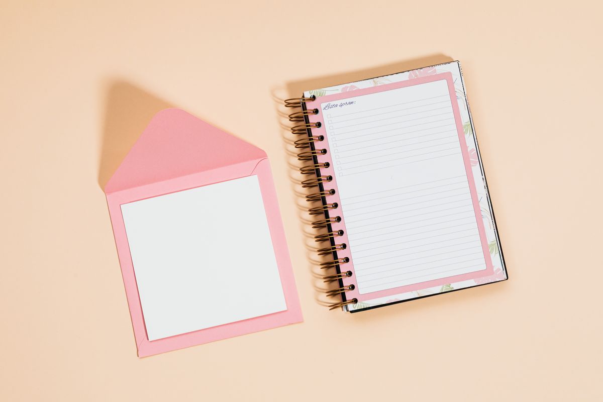 A flat lay of a pink notebook and envelope on a peach background, offering ample copyspace.