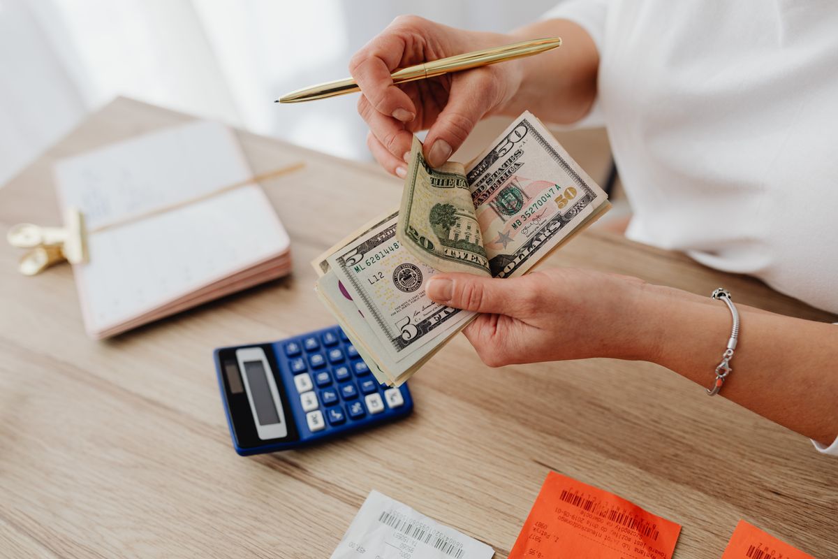 Woman counting cash with a calculator at a desk, managing finances.