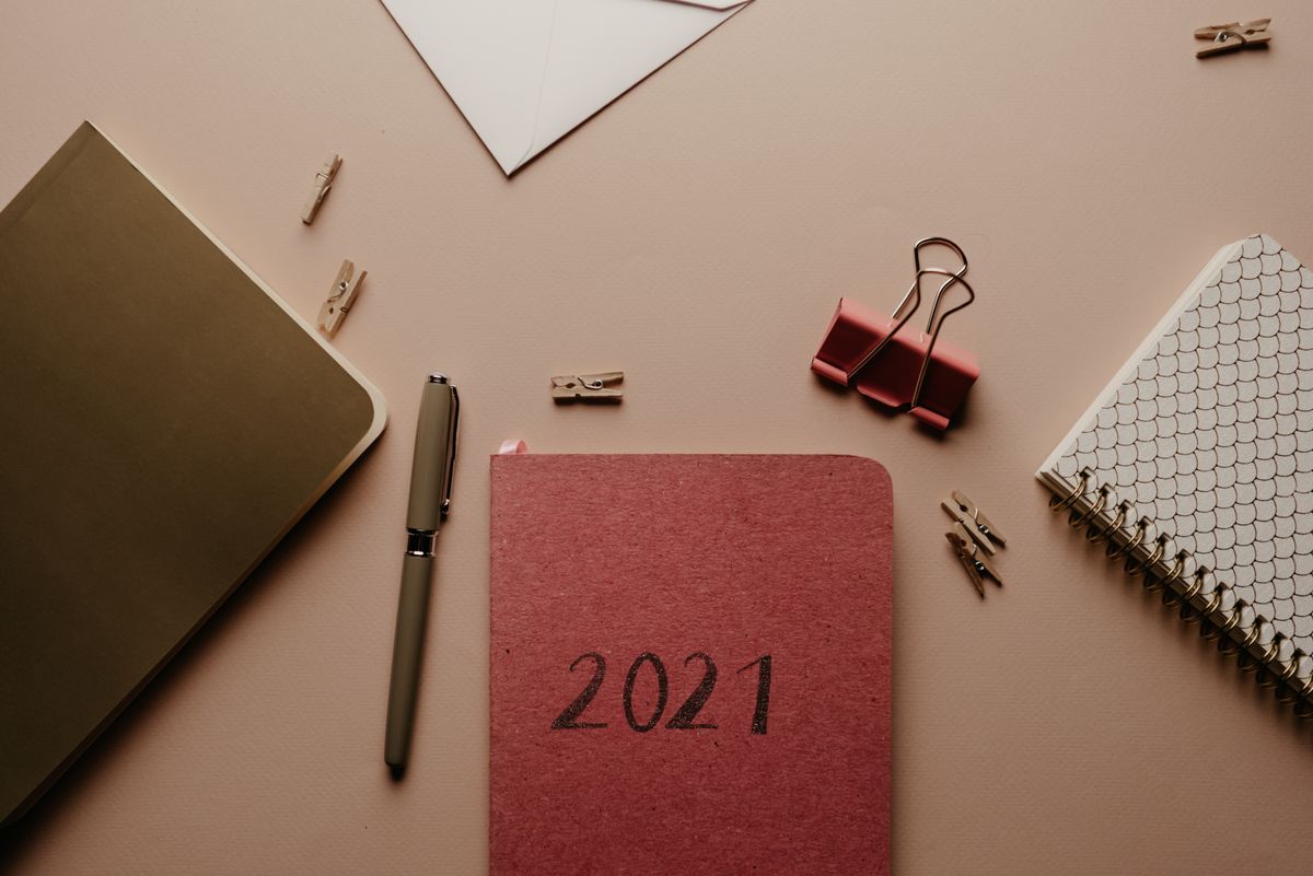 Top view of a 2021 planner with office supplies arranged on a desk for organization.