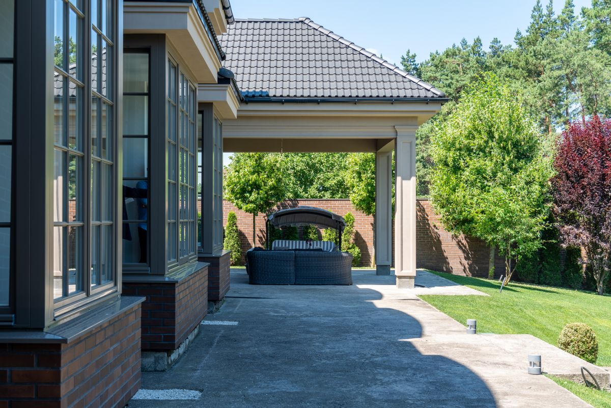 Relaxing patio with modern furniture, garden view, and tiled roof in a summer setting.