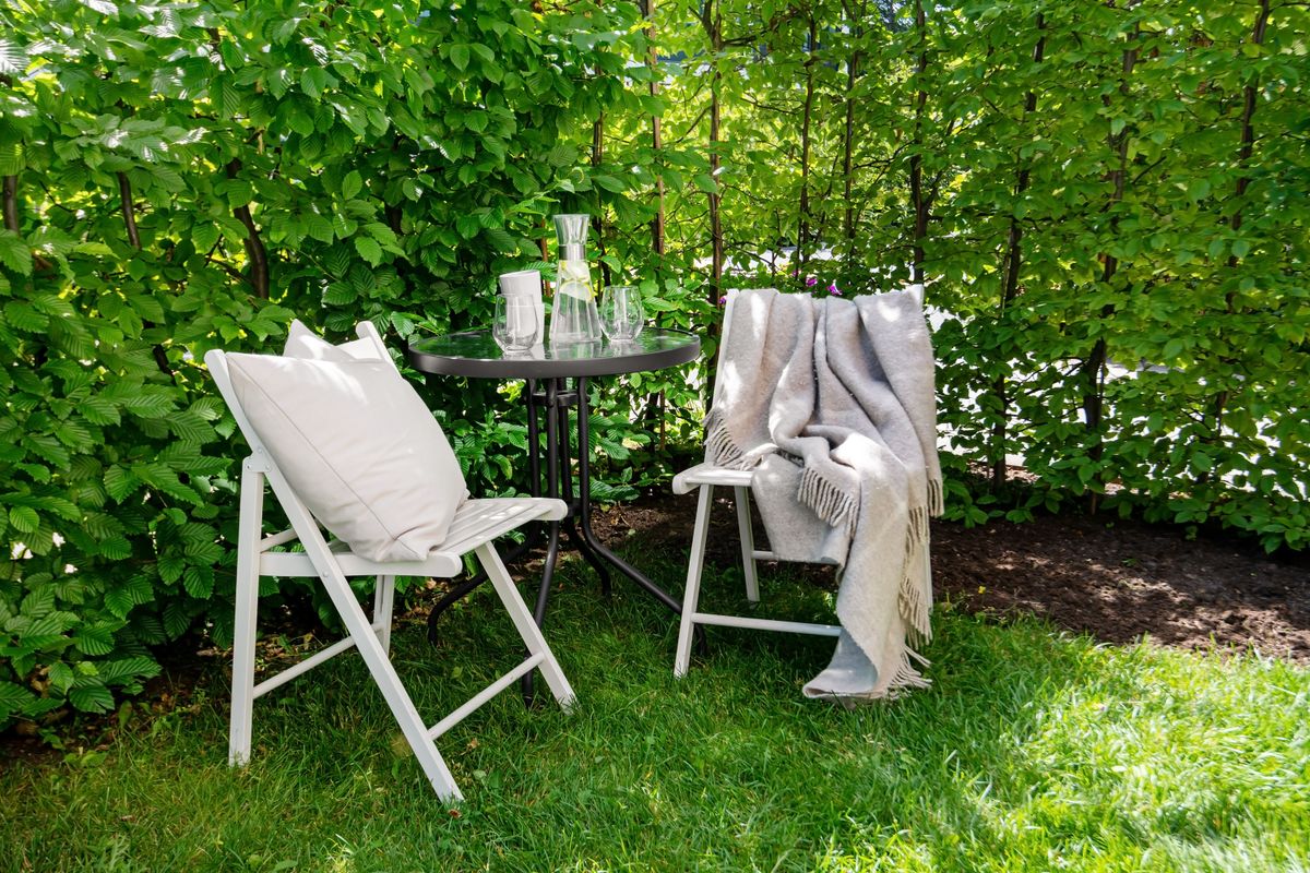Relaxing outdoor patio setup with chairs, table, and green garden backdrop.