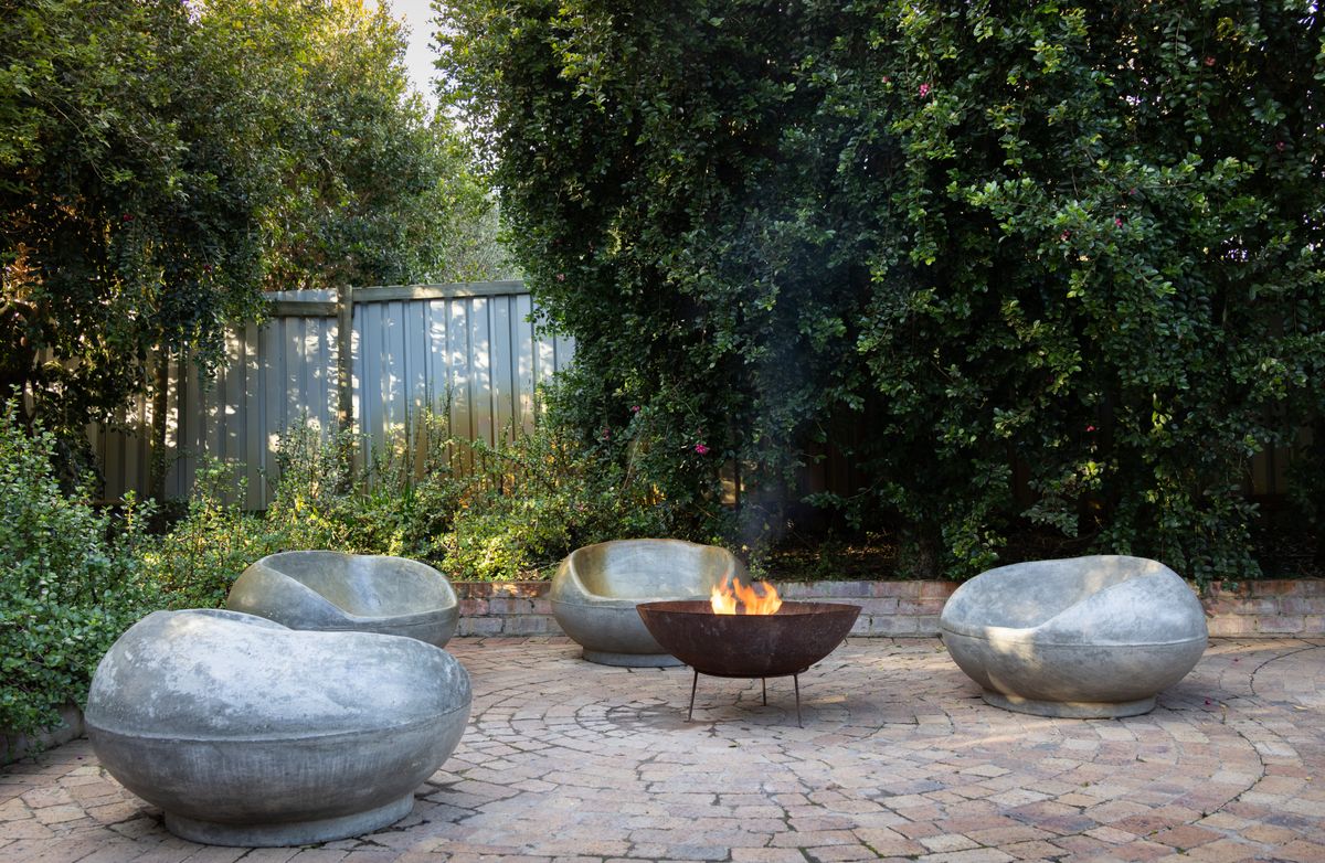 Cozy backyard seating area with modern stone chairs around a fire pit.