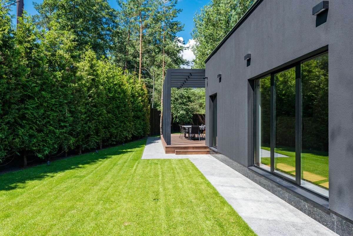 Stylish modern house exterior with a lush green yard and outdoor seating area.