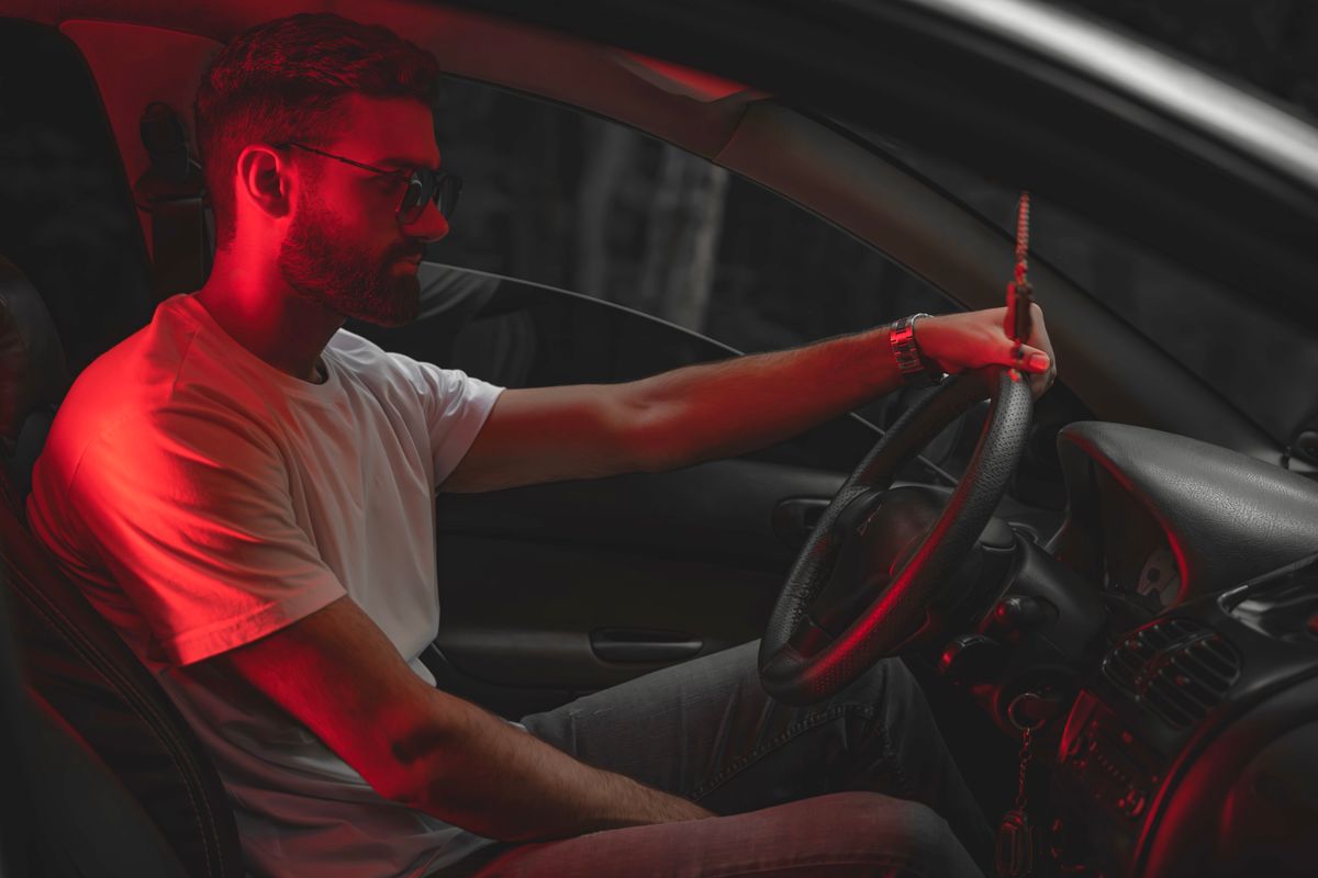 Man in sunglasses driving car, illuminated by red light, nighttime vibe.