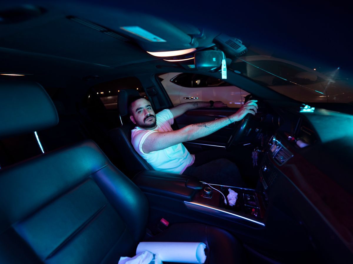 Man driving a car at night in Baghdad, illuminated by interior lights with a modern car interior.