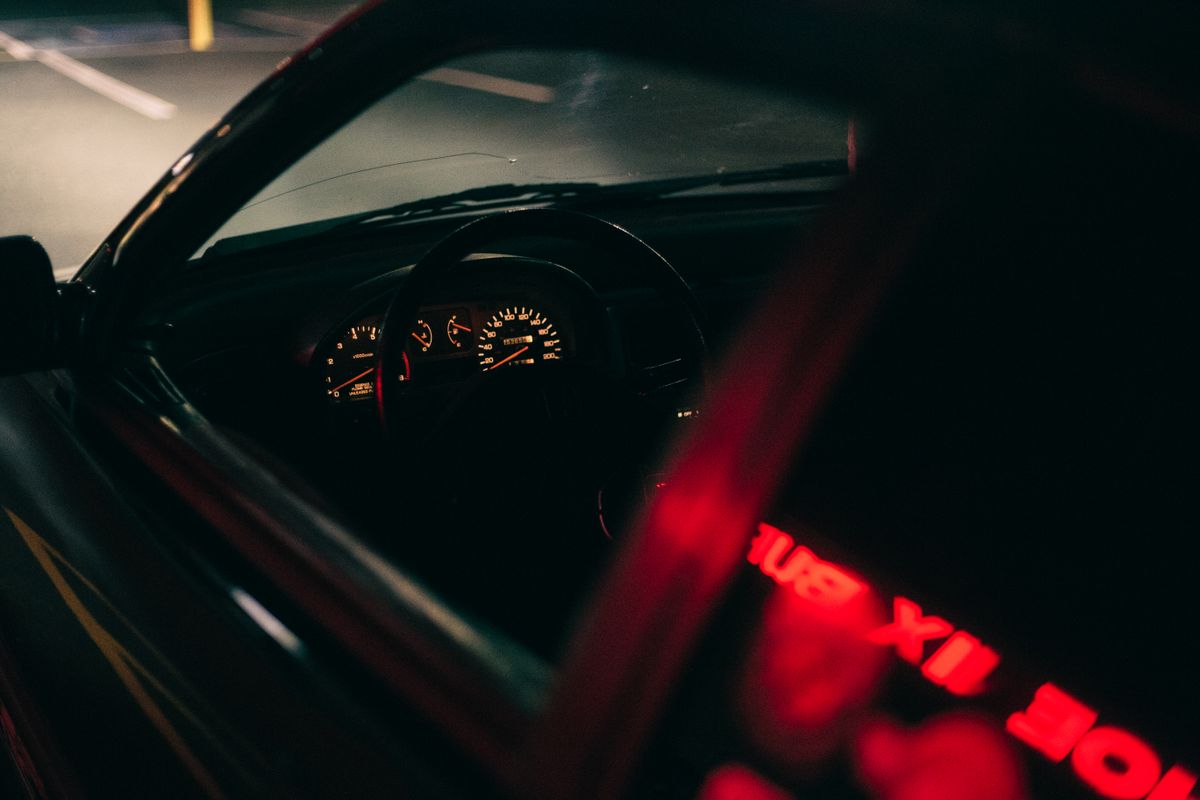 Moody view of a dimly lit car interior at night with dashboard lights and street reflections.