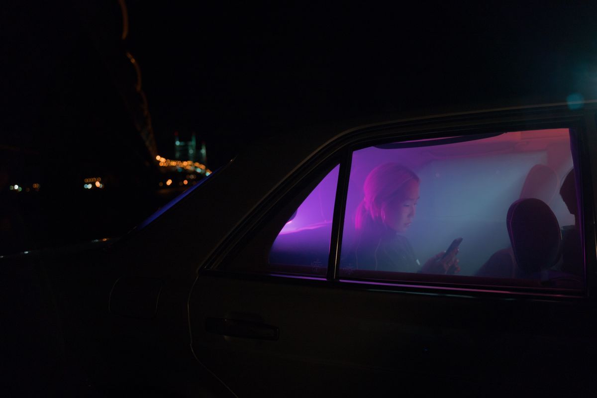 Moody shot of a person using a smartphone in a car with neon lights during night travel.