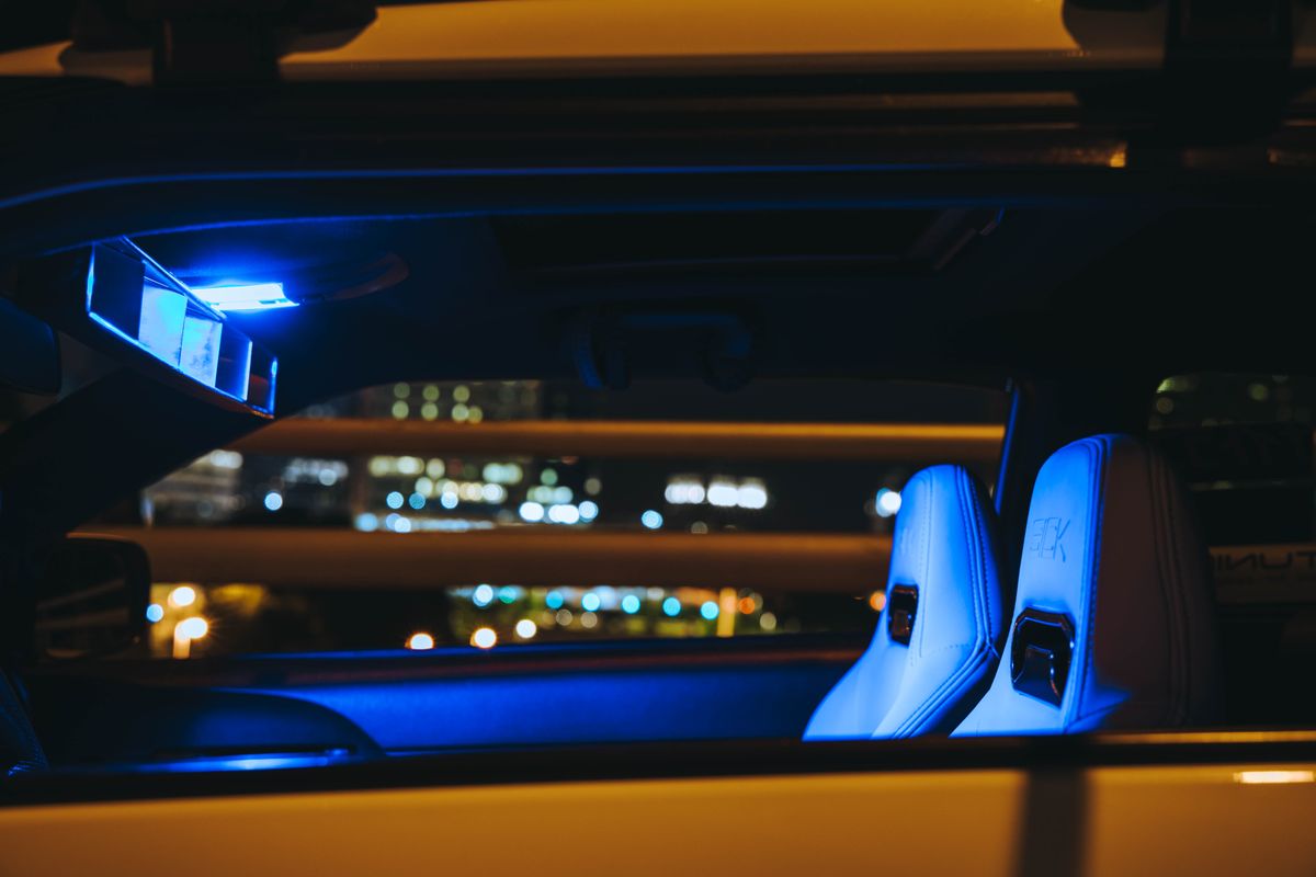 Car interior illuminated by blue light, showcasing modern seats against a city backdrop at night.