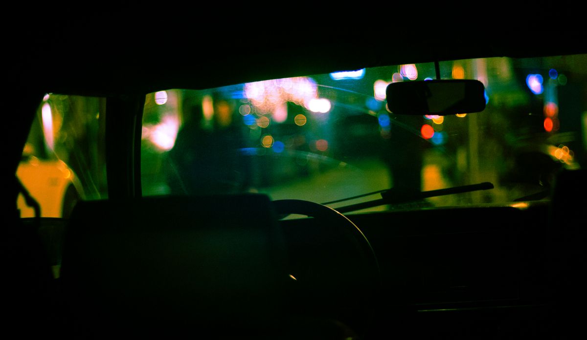 View from the passenger seat through windshield of city with glowing lights on blurred background parked on street at night time