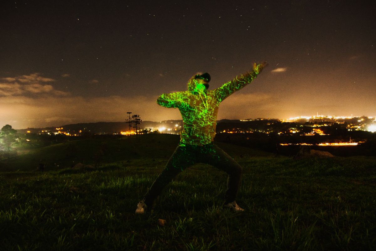 A person dances energetically under the stars with neon lights at night in a field.