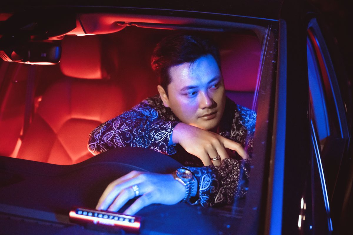 A young man in a car with neon red and blue lights creating a dramatic mood.