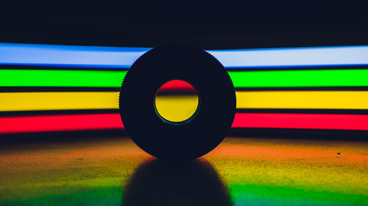 Round disk placed on black surface against abstract background with creative colorful rainbow lights in dark studio with dim light