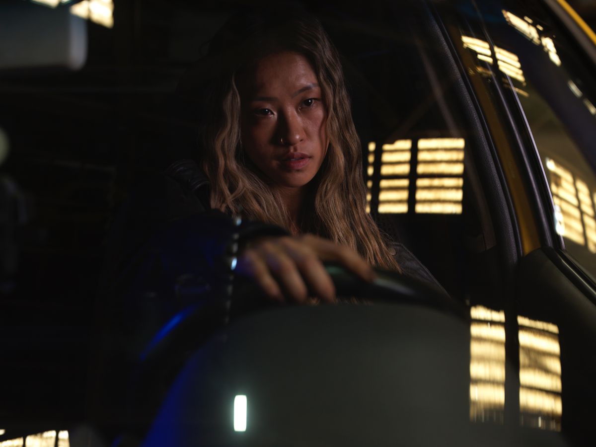 A young woman with a nose ring drives at night, illuminated by city lights.