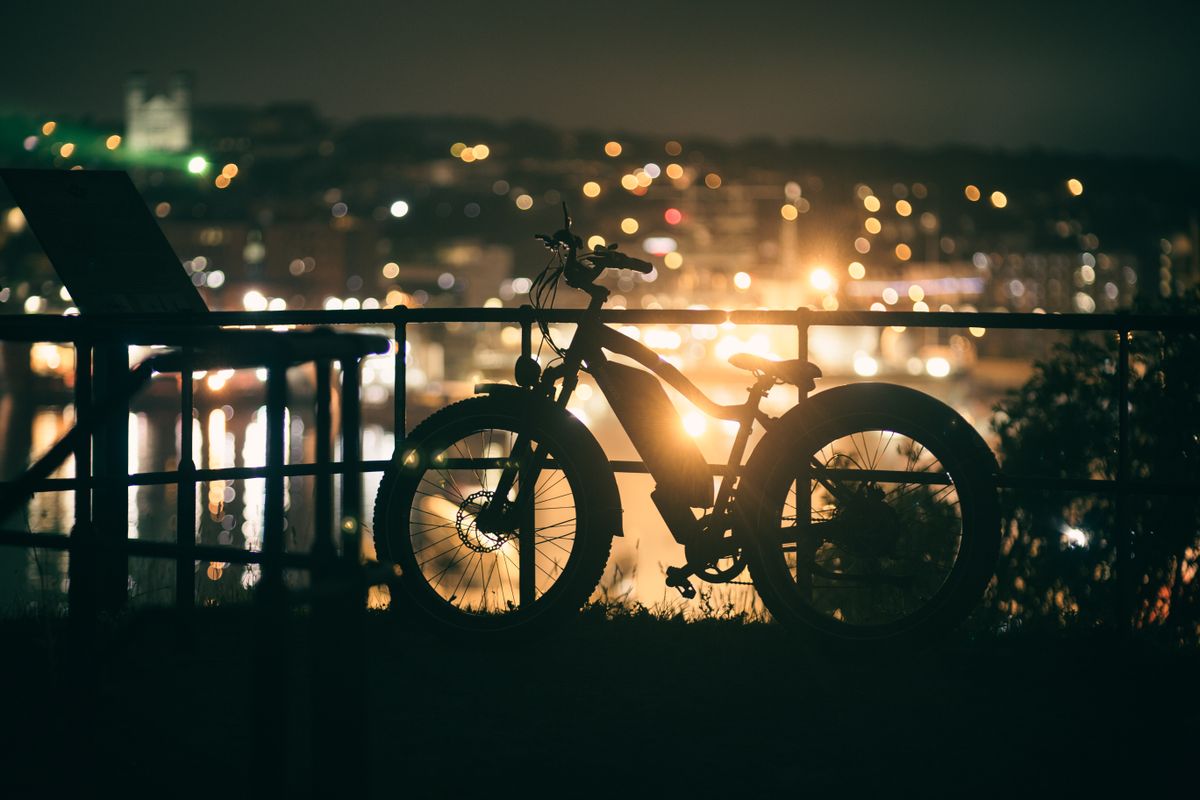 A bicycle silhouette against vibrant city lights captures a serene urban night scene.