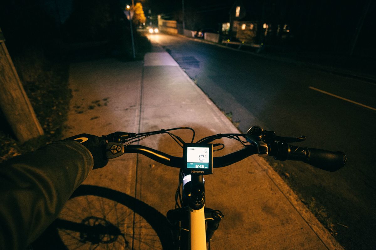 Cyclist's perspective riding at night on a dimly lit road with digital display on handlebars.