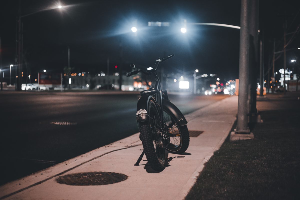 A bicycle parked on a sidewalk at night in an urban setting, showcasing city lights.