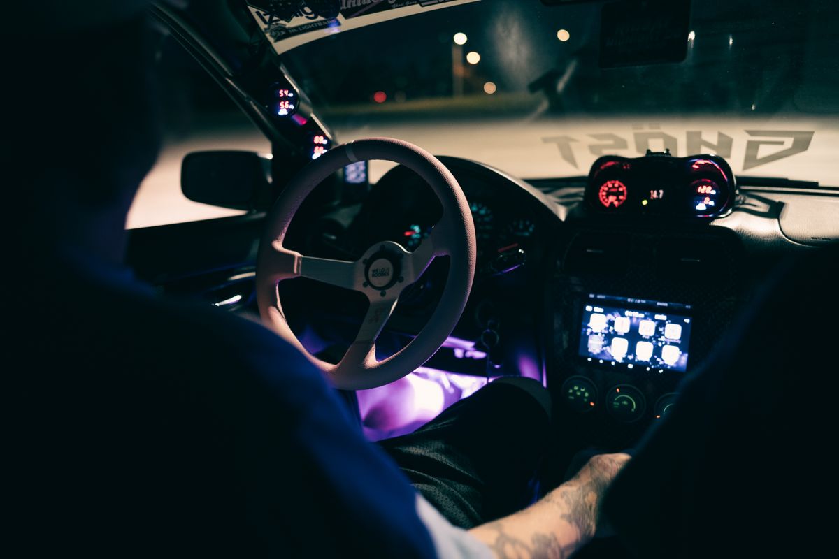 A car interior at night with a brightly lit dashboard and steering wheel, showcasing modern technology.