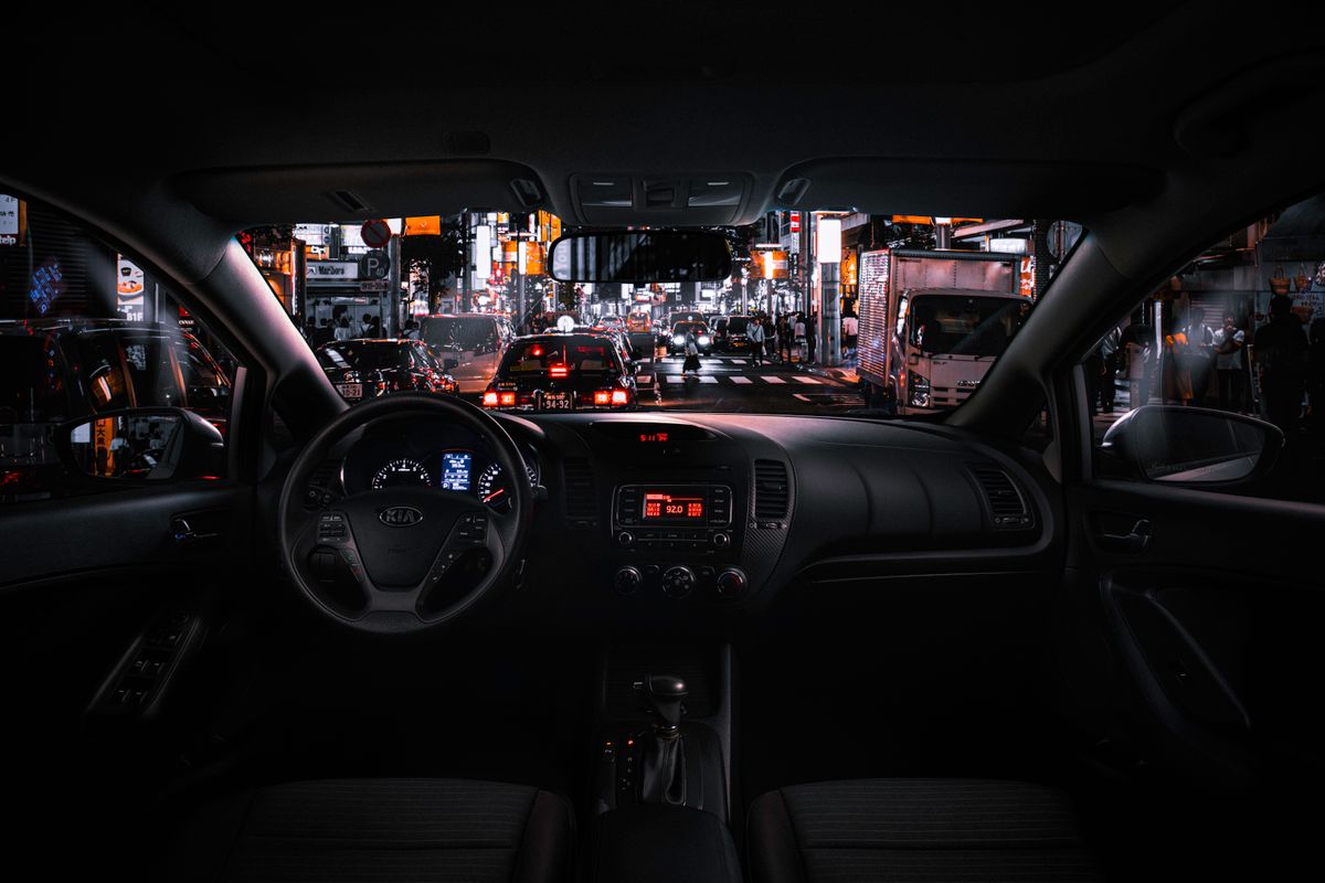 View from car interior at night in Tokyo, featuring bustling street traffic and illuminated cityscape.