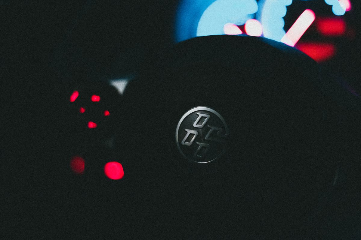 Close-up view of a car steering wheel and dashboard with vibrant instrument lighting in a dark setting.
