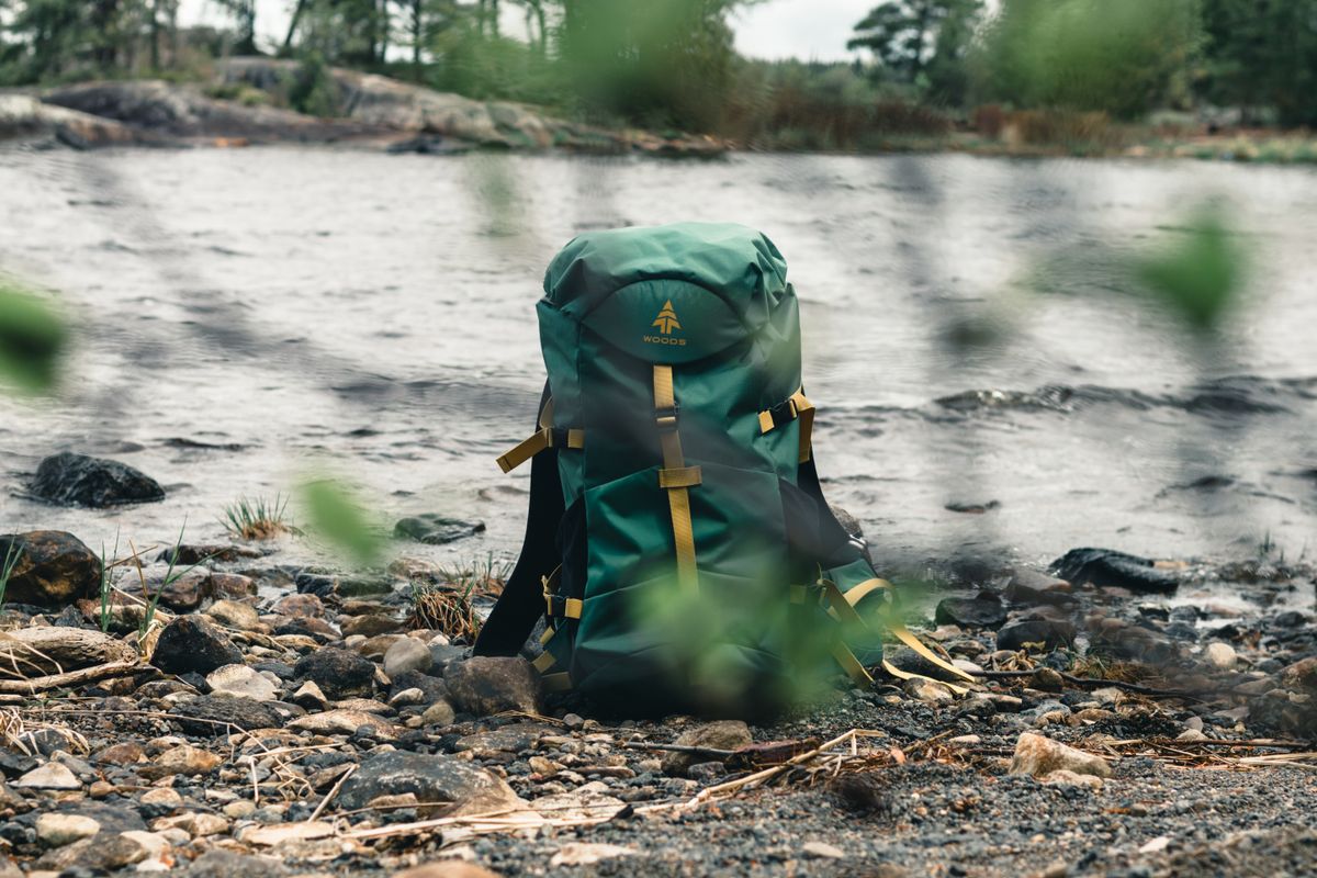 Green backpack by a rocky lakeside in Saint-Henri-de-Taillon, QC, Canada, ideal for nature adventures.