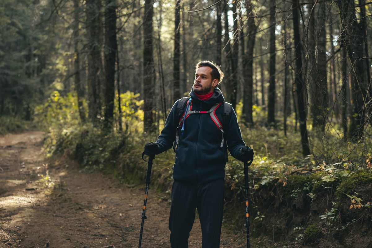 A man hiking in a sunlit forest, enjoying an outdoor adventure with trekking poles and a backpack.