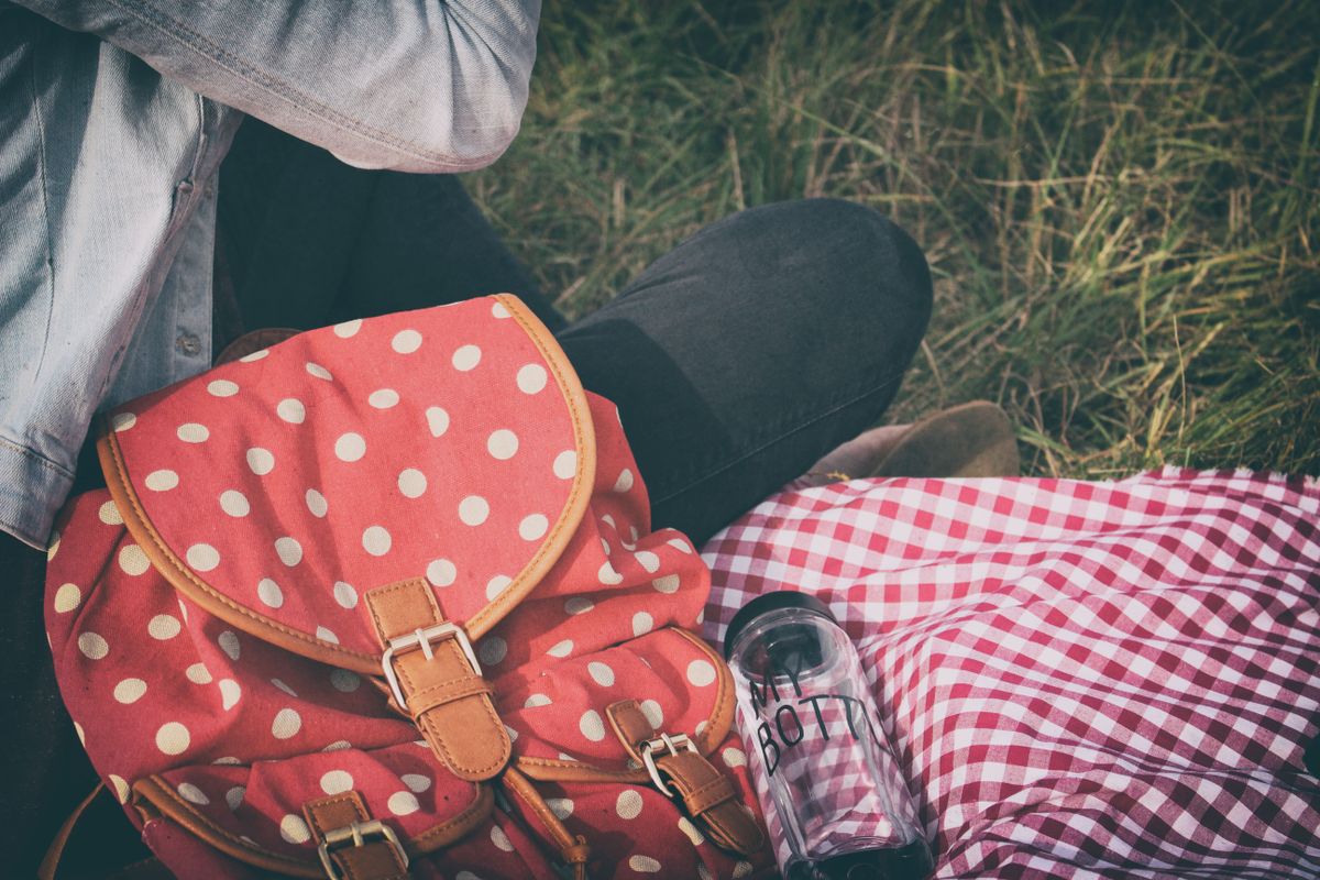 Charming outdoor picnic setup with a red polka dot bag and checkered blanket on the grass.