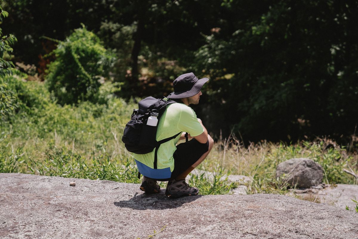 A man in a yellow shirt and black hat enjoying a serene outdoor hike.