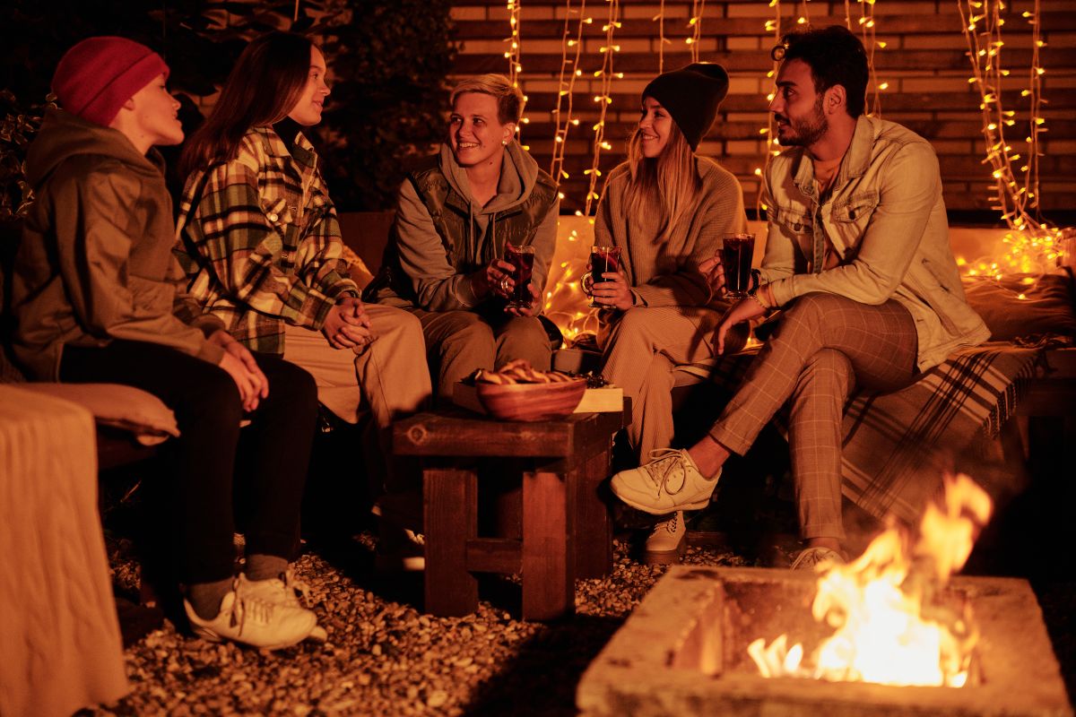 A group of friends enjoying a warm outdoor bonfire, sharing drinks and laughter at night.