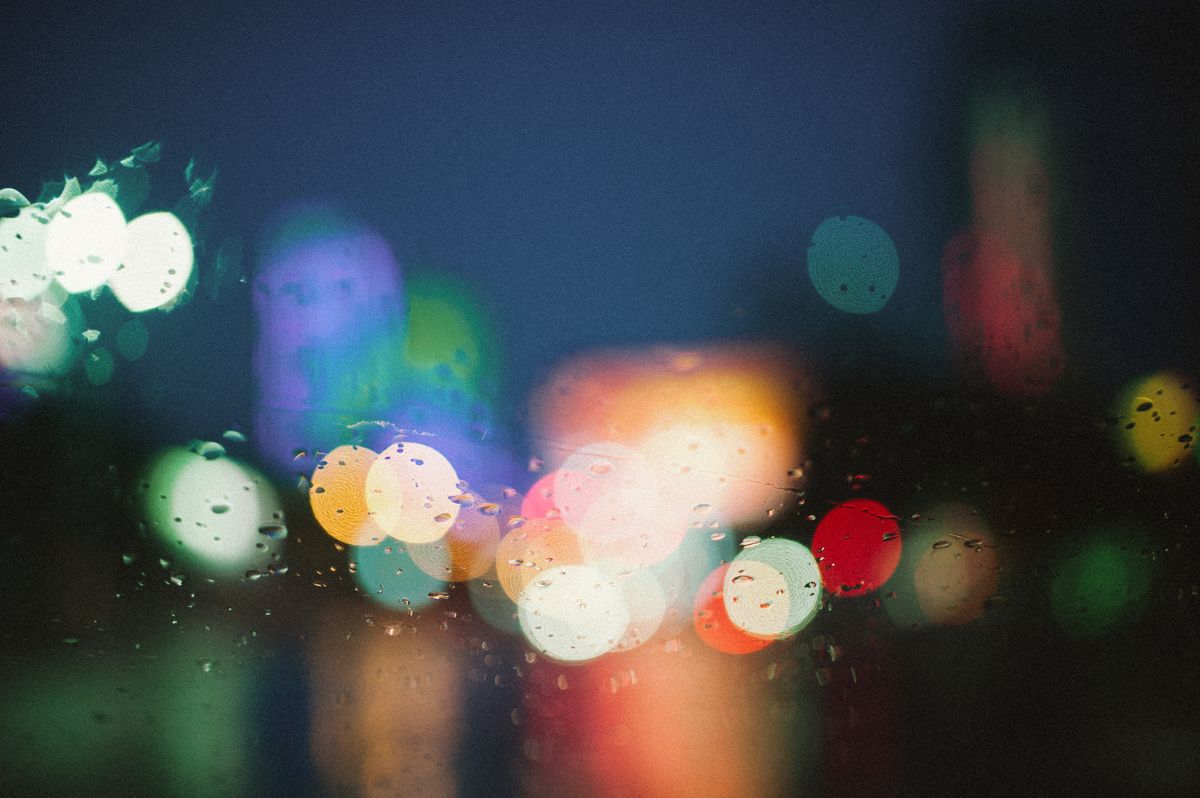 Colorful city lights create a vibrant bokeh effect on a rainy night, creating a dreamy and artistic atmosphere.