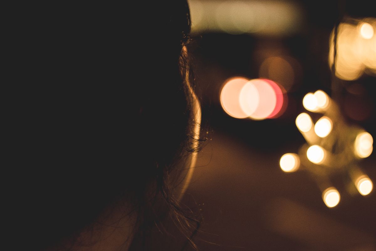 Silhouette of a woman with blurred golden bokeh lights at night creating a warm, moody atmosphere.