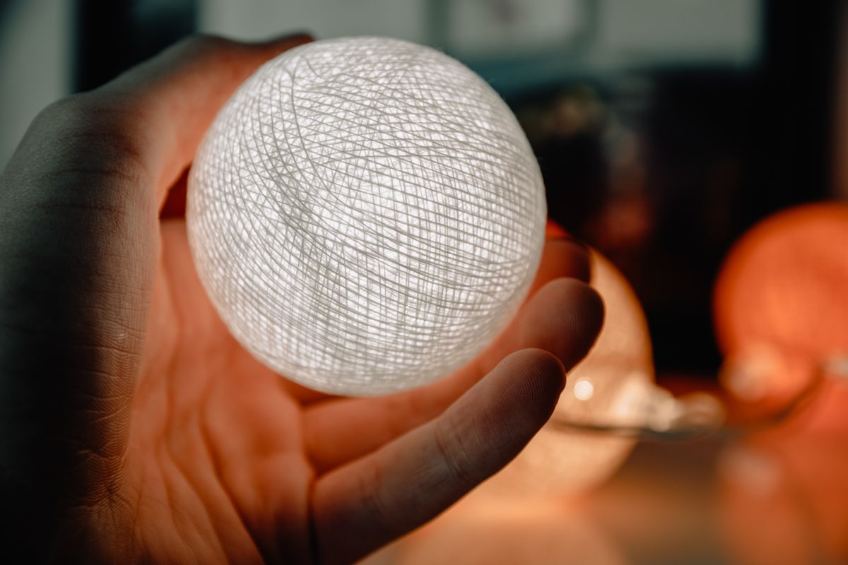 Close-up of a hand holding an illuminated sphere light indoors, creating a warm, moody atmosphere.