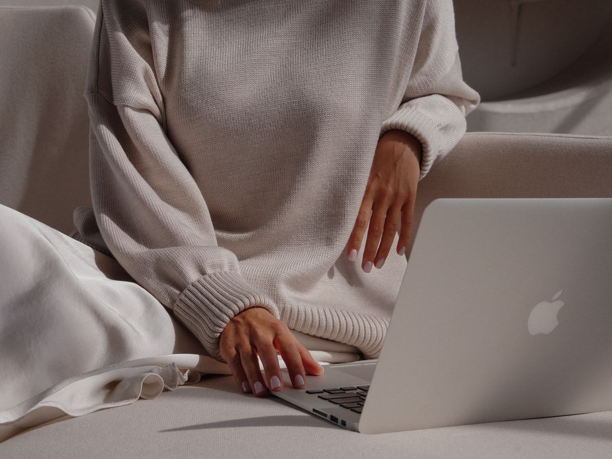 Woman in a cozy sweater using a laptop, showcasing a relaxed and fashionable lifestyle.