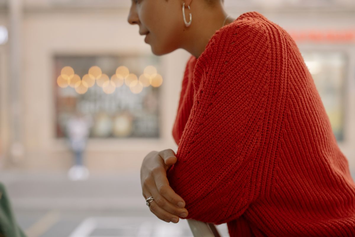 Side profile of a woman in a vibrant red knitted sweater with blurred urban background.