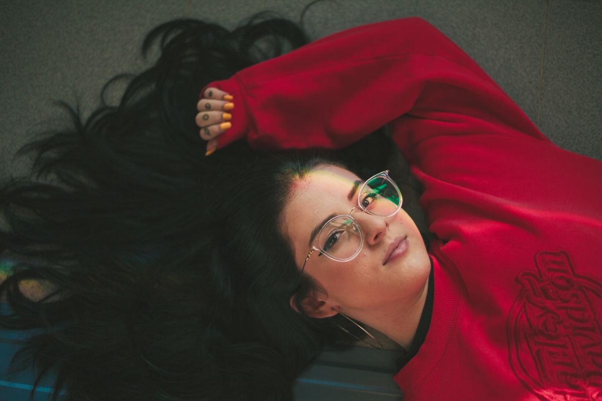 Portrait of a woman with glasses and long hair wearing a red sweater, lying down indoors.