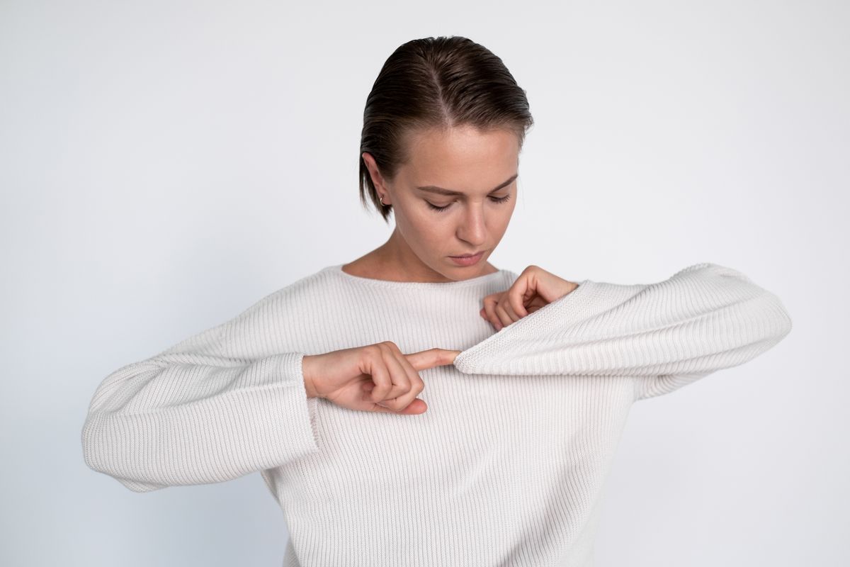 Portrait of a woman wearing a white sweater, closely examining her sleeve.