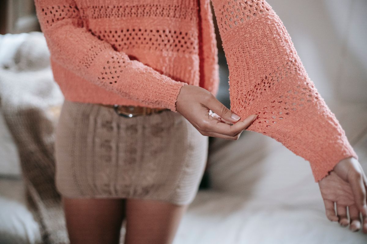 High angle of crop anonymous ethnic female wearing knitted sweater and skirt demonstrating quality of clothes