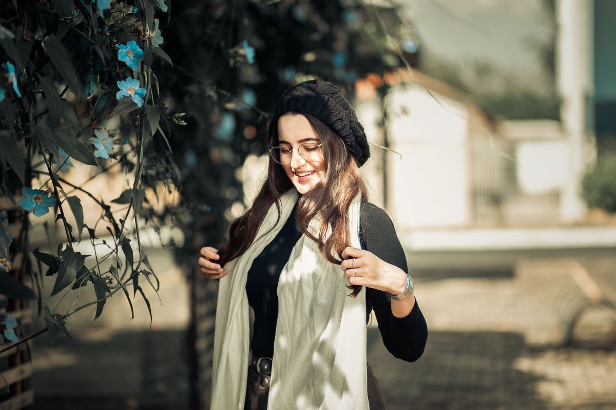 Woman wearing black outfit and glasses, surrounded by blue flowers outdoors.