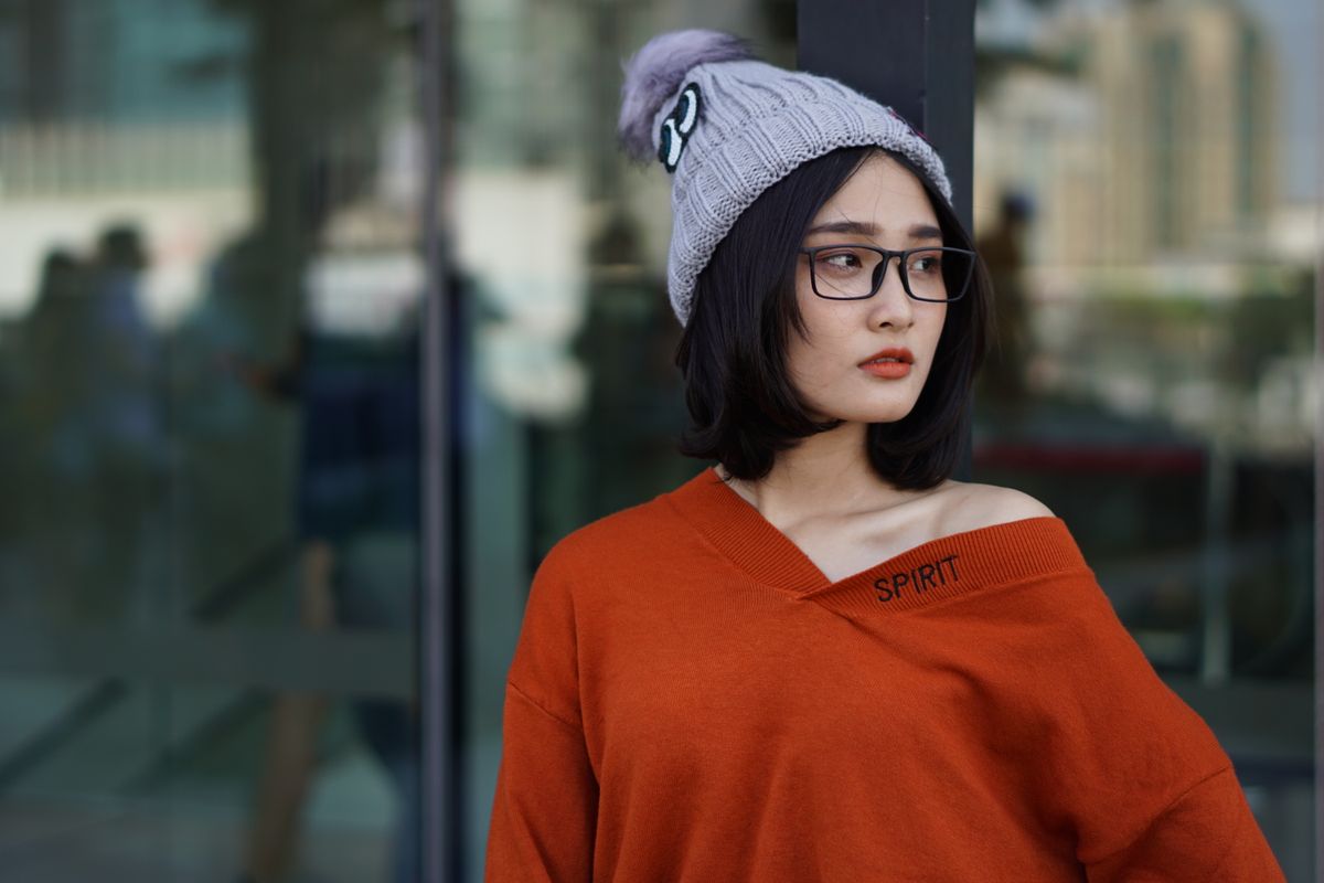 Fashionable woman poses outdoors in an orange sweater and knit hat, exuding modern style.