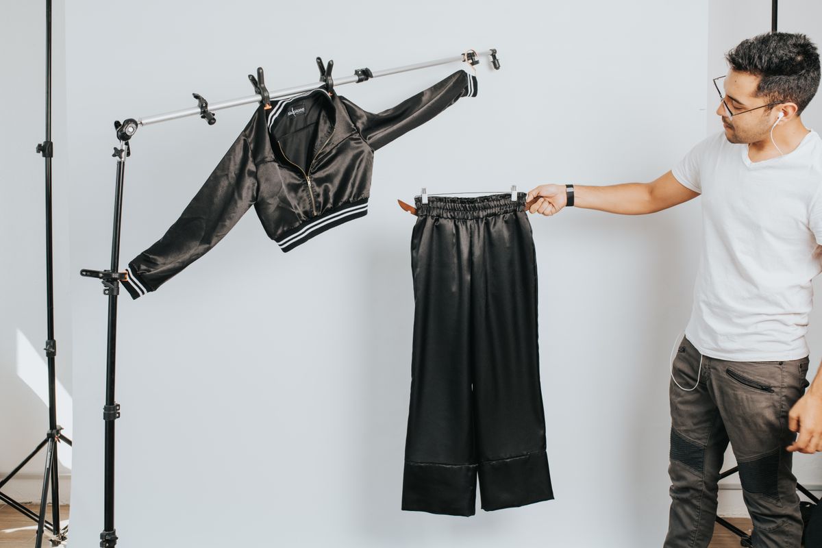 A man arranging a stylish black outfit in a studio setting, showcasing modern fashion.