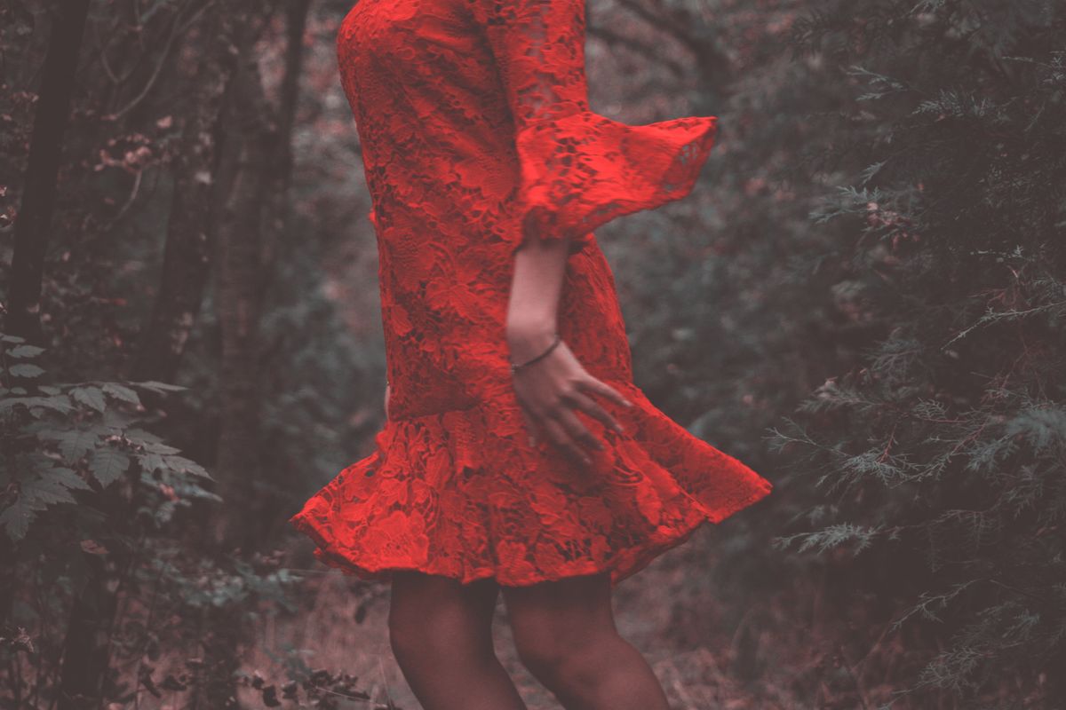 Elegant woman in a red lace dress positioned in a serene wooded area.