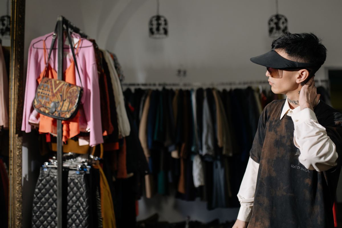 Man wearing sunglasses and sun visor browsing clothes rack at thrift store.