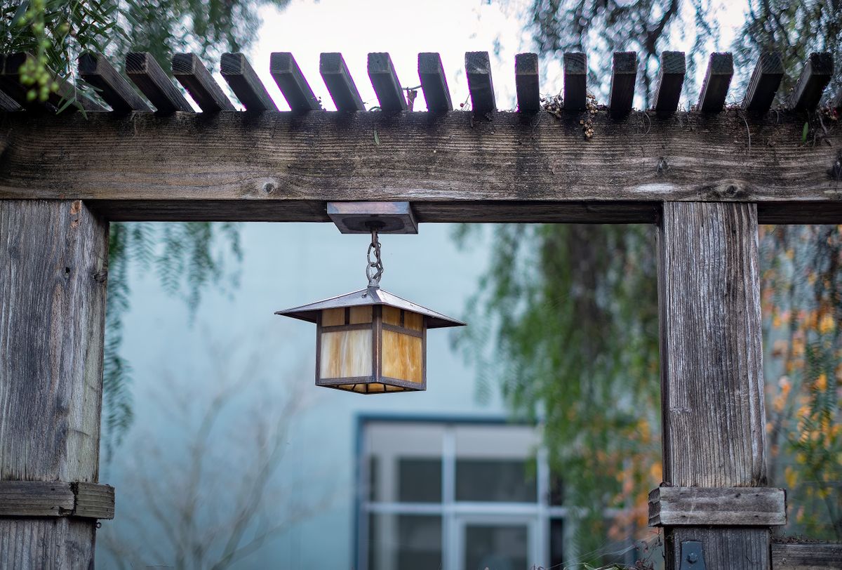 A vintage lantern hangs from a rustic wooden arbor in a tranquil garden setting.