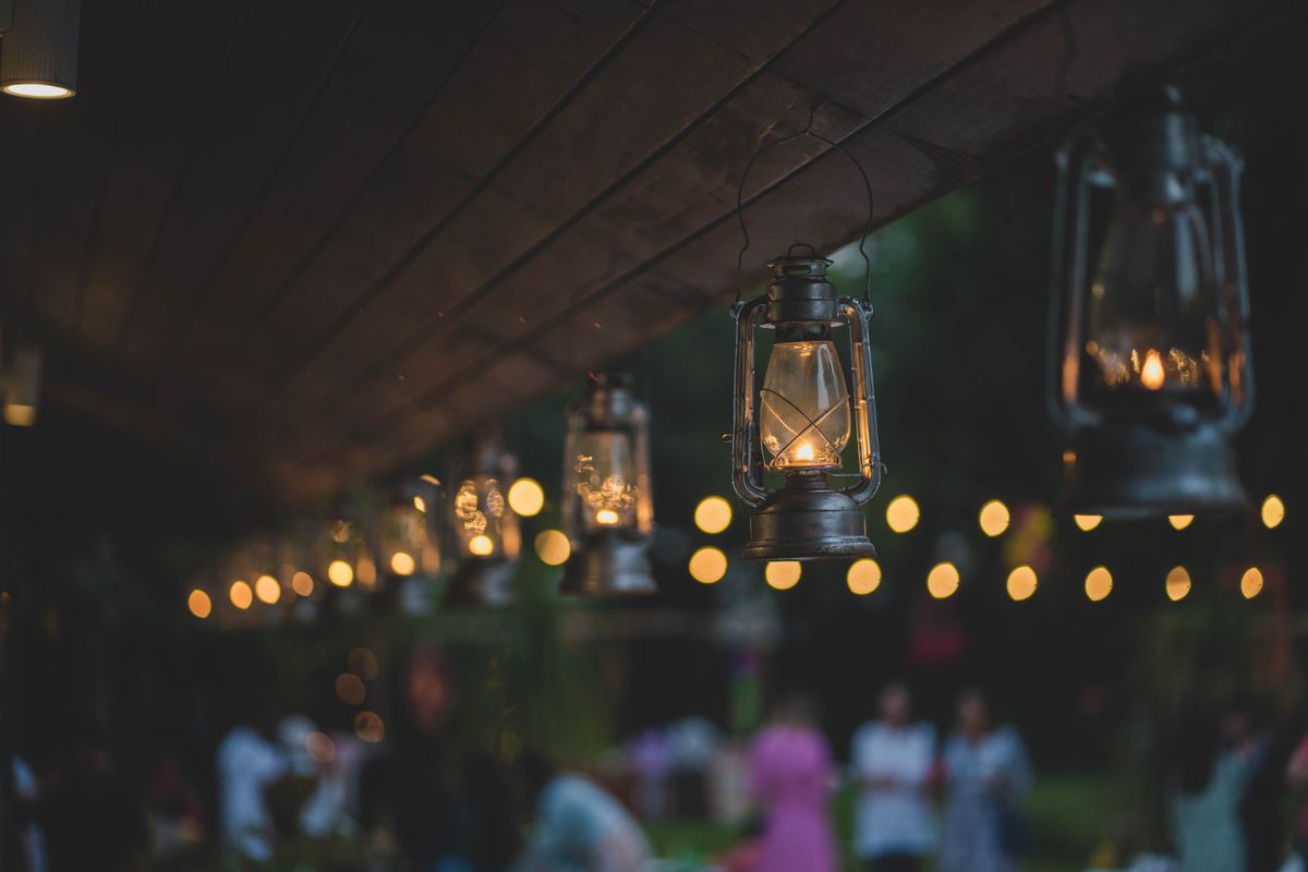 Charmingly lit oil lamps hanging from a wooden ceiling at a vibrant outdoor evening gathering.