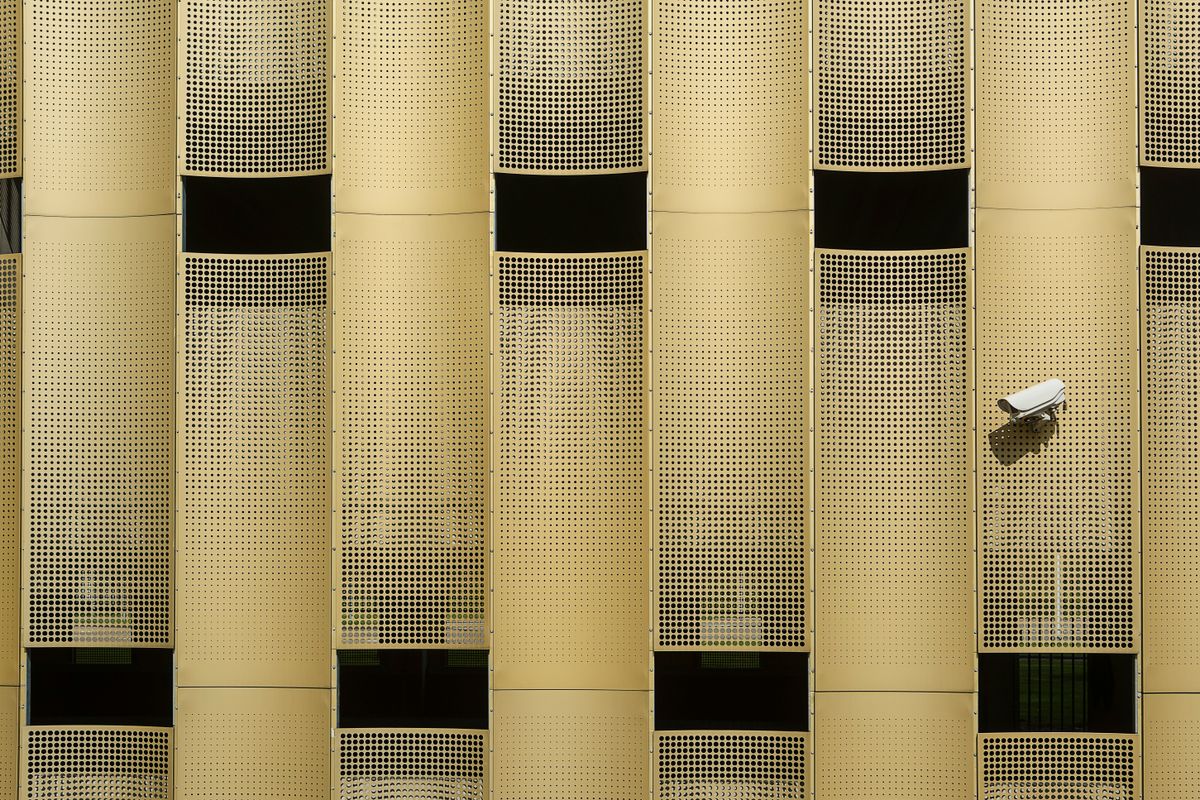 Close-up of a modern building facade with a prominent CCTV camera, showcasing architectural design.