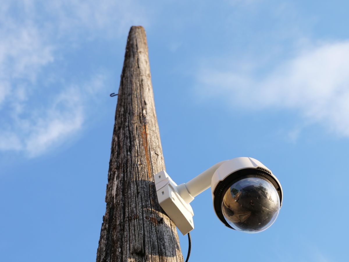 A security camera mounted on a wooden pole against a clear blue sky, highlighting urban surveillance.