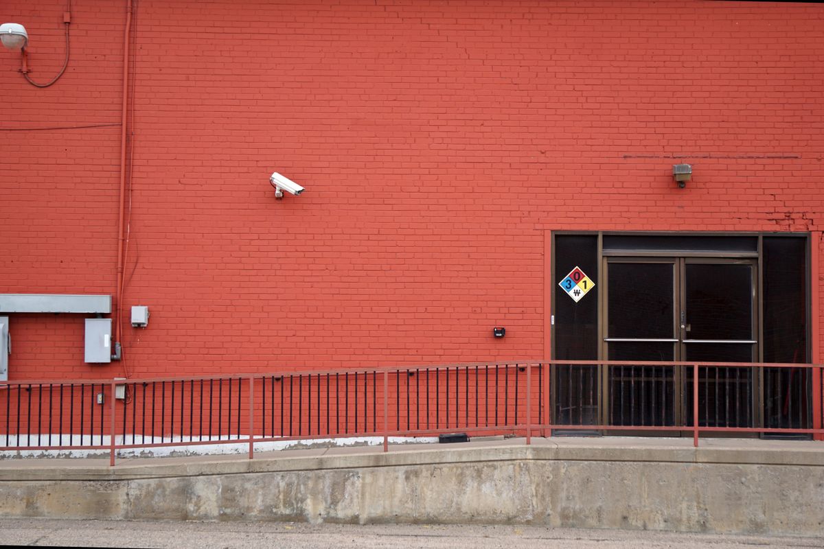 Urban red brick wall with security camera and entrance, featuring safety signage and railing.