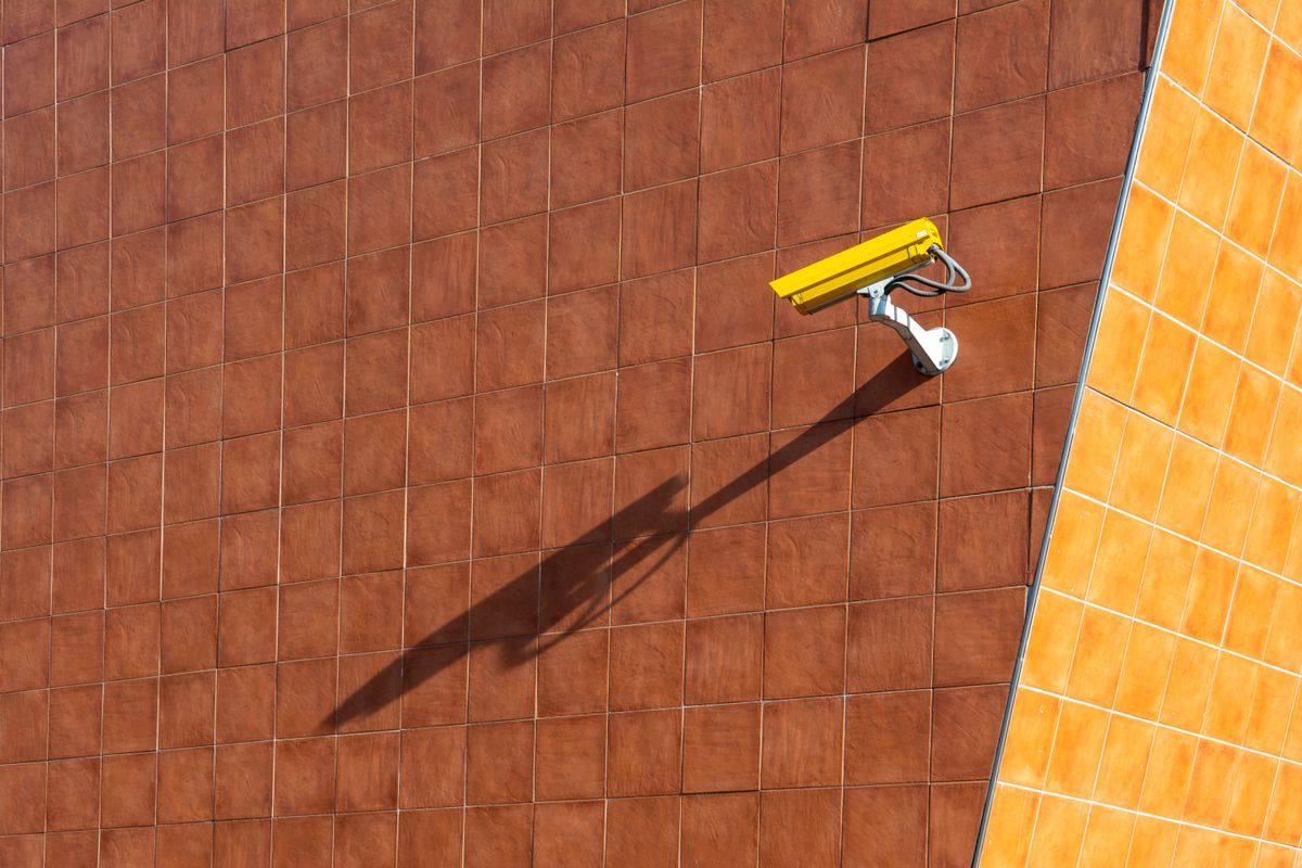 Security camera casting a shadow on an orange and brown tiled wall.